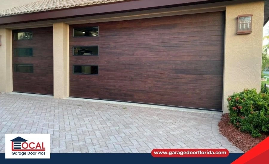 A modern, dark gray, two-car garage door with windows, installed on a well-maintained suburban home in Tampa, FL, representing a long-lasting and durable garage door.