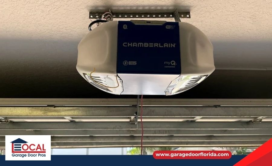 A Chamberlain myQ garage door opener mounted on a ceiling, looking out towards an open garage door revealing a suburban street with cars.