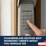 A person's finger pressing a button on a Chamberlain wireless garage door keypad mounted outside.