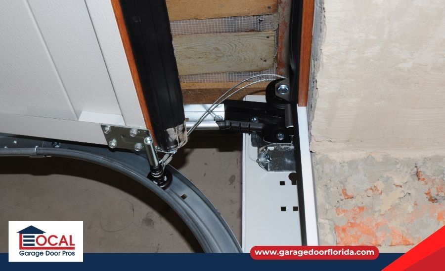 Close-up of a garage door's upper track, roller, and metal lifting cable mechanism, featuring a Local Garage Door Pros logo.
