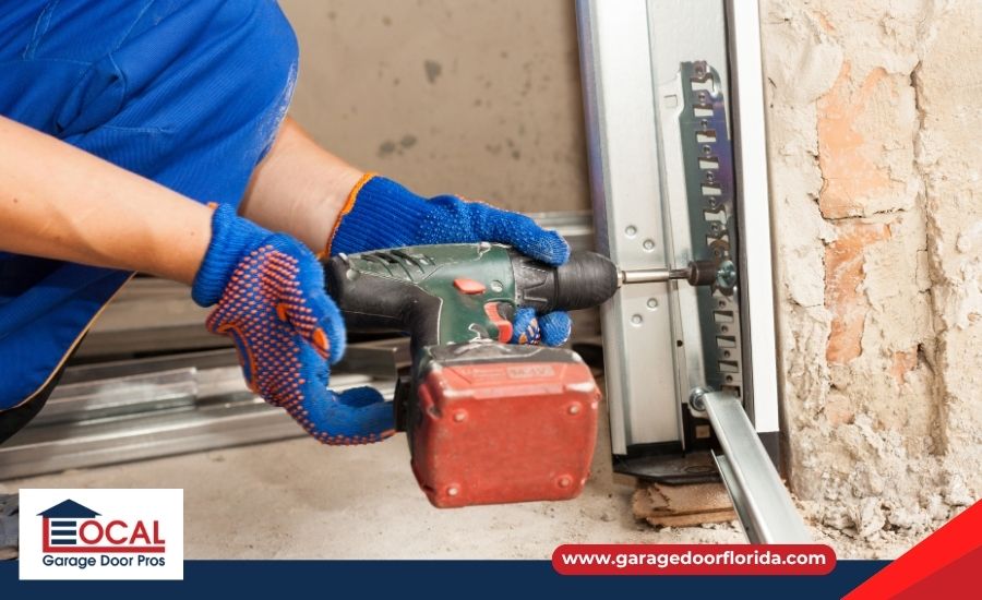 A worker wearing blue gloves using a power drill to adjust the metal track near the bottom of a garage door.