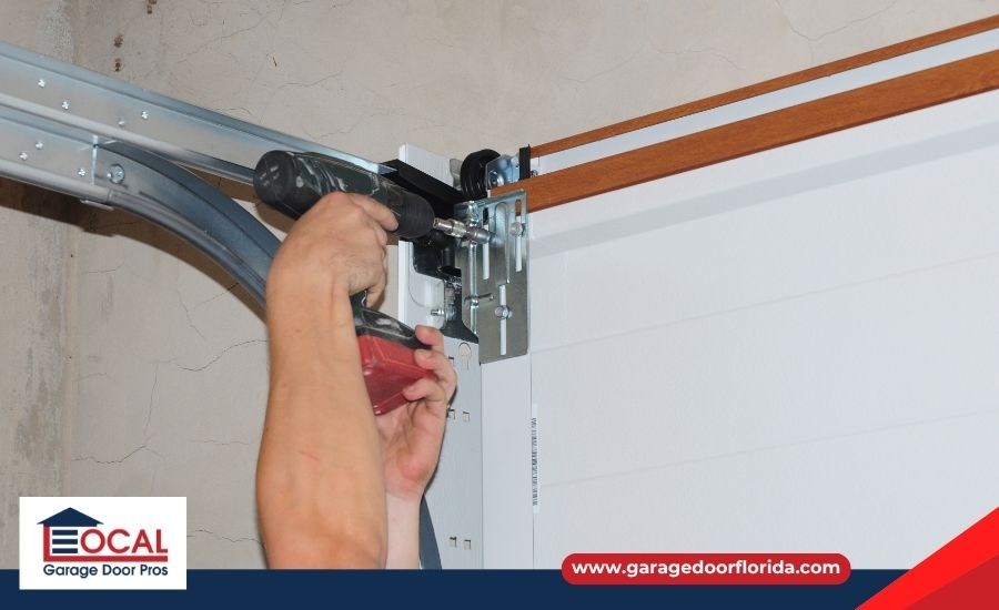 A worker using a power drill to install or repair a top metal bracket on a white garage door.
