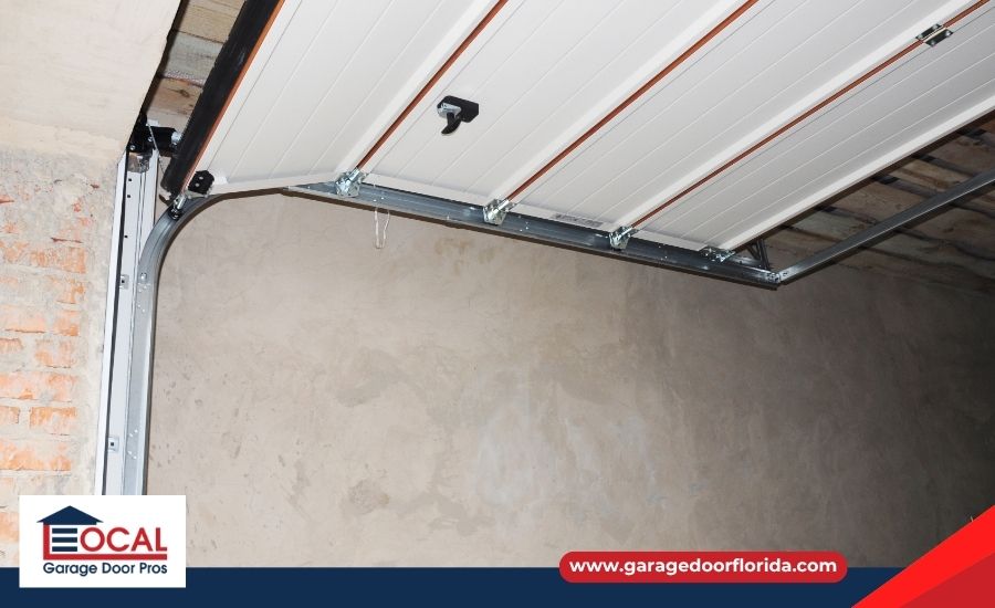 A partially open white paneled garage door resting on its curved metal tracks inside an unfinished garage.